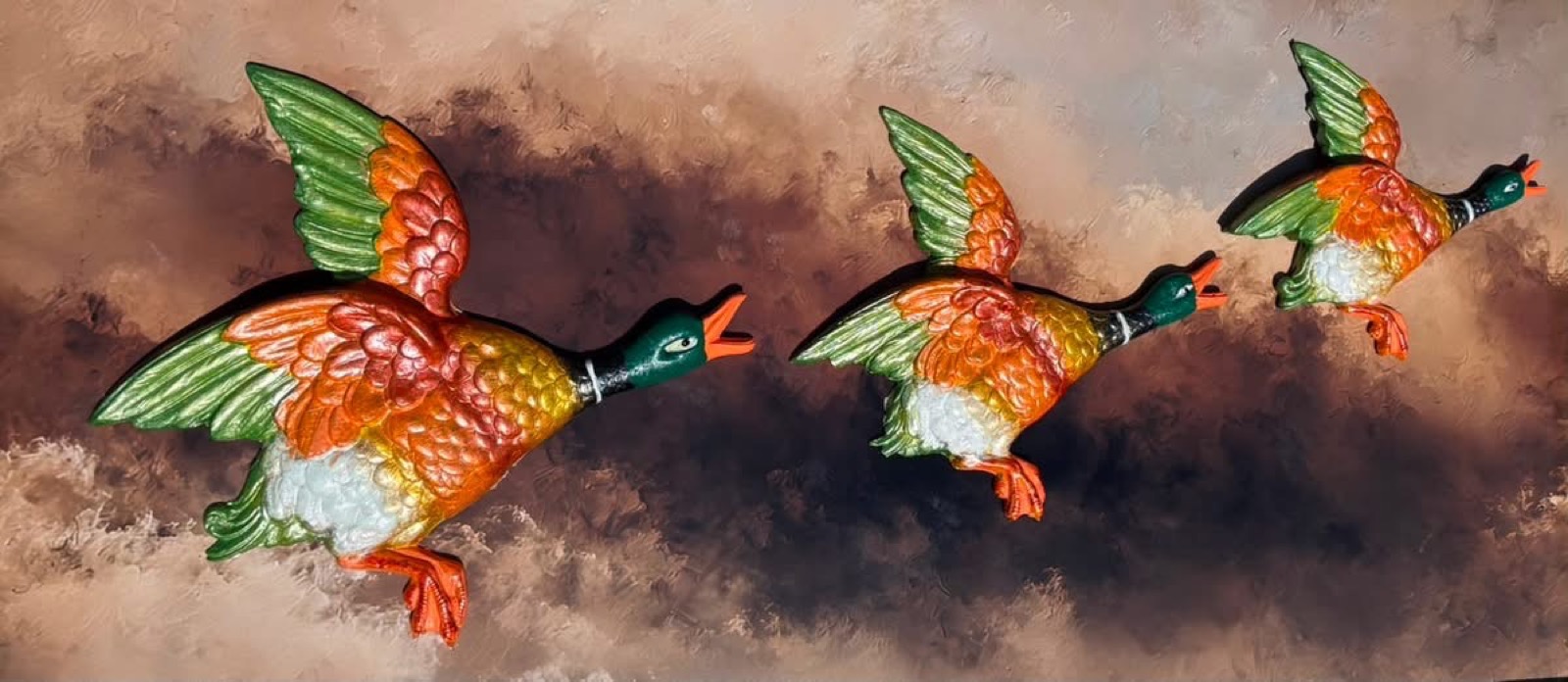 Three brightly painted ducks flying across a painted sunset sky