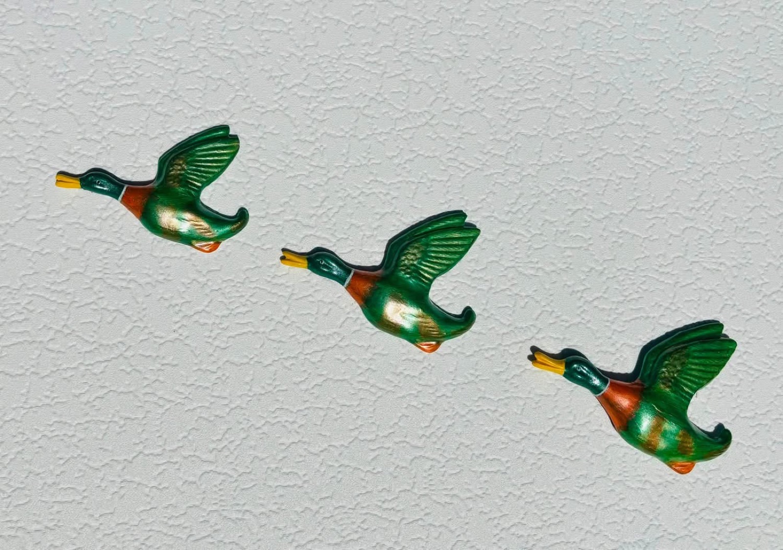 Set of three handmade flying ducks in emerald green and orange, climbing a white wall