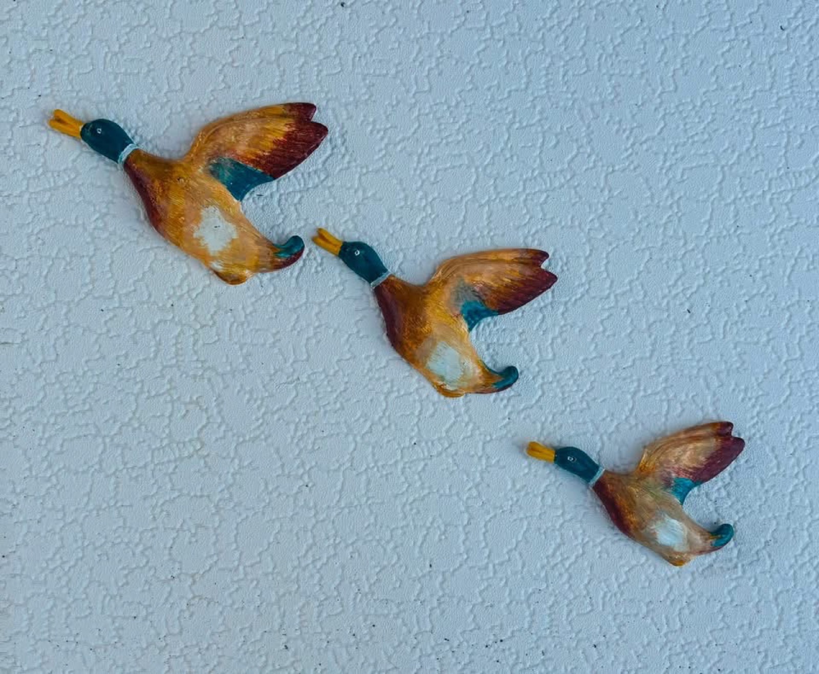 Three flying ducks painted in soft teal, apricot and cream