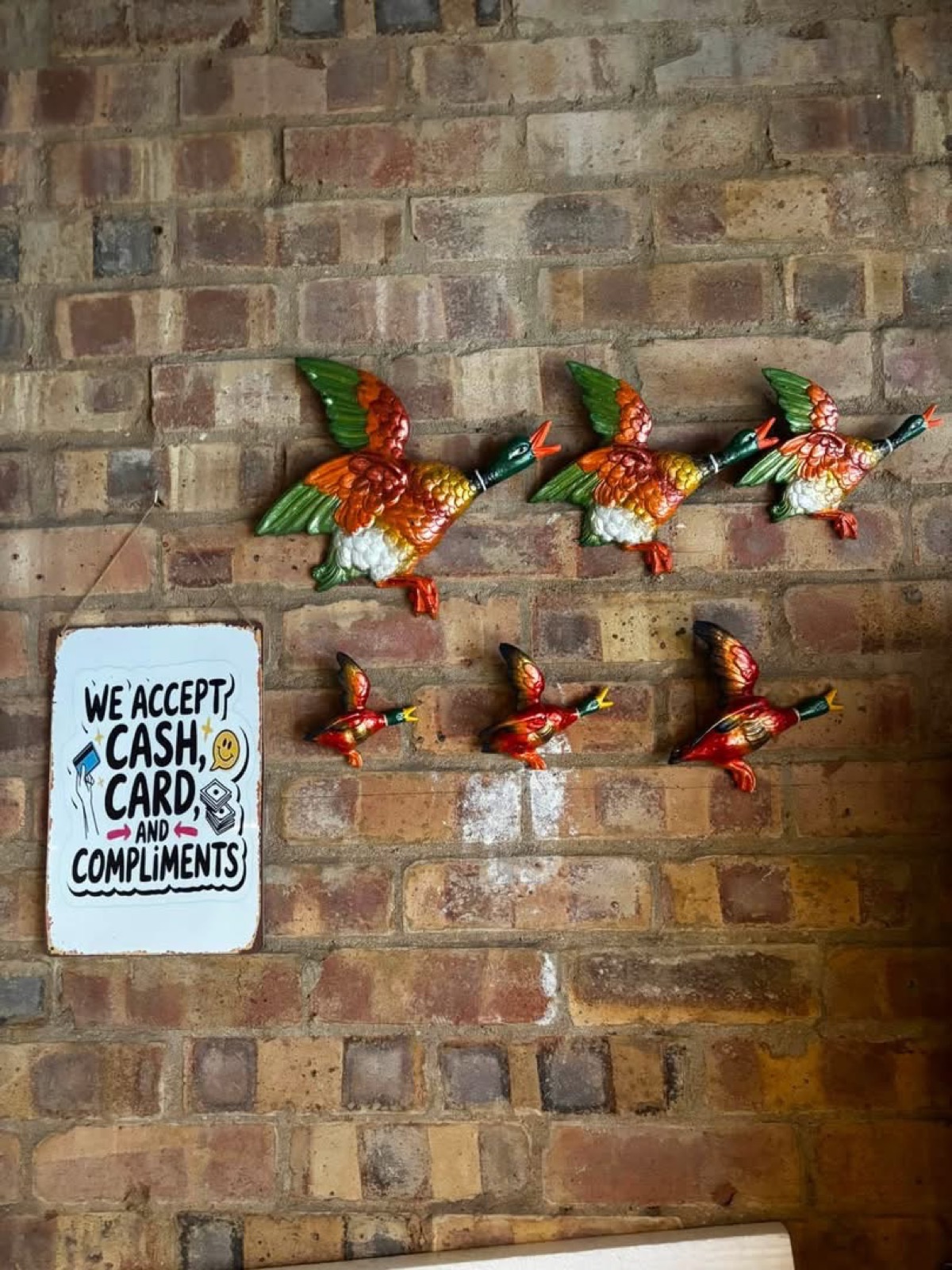 Two sets of handmade flying ducks hung on a brick wall, a large set above a smaller set
